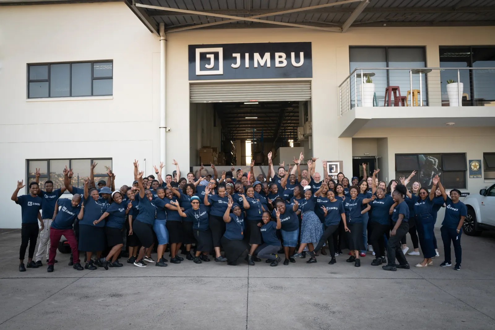 The whole JIMBU team in navy JIMBU T-shirts celebrating outside the JIMBU building