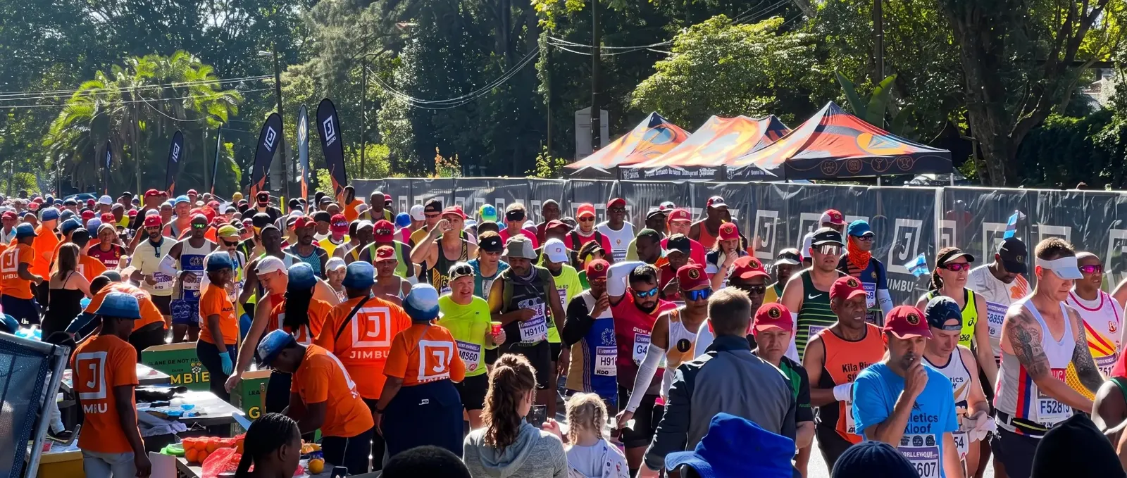 JIMBU team in orange branded shirts at a water table with runners at the Comrades Marathon